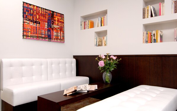 A modern living room with a white sofa, a coffee table with newspapers, a vase with flowers, and bookshelves with books. - Hotel Villa Pannonia (Venice)