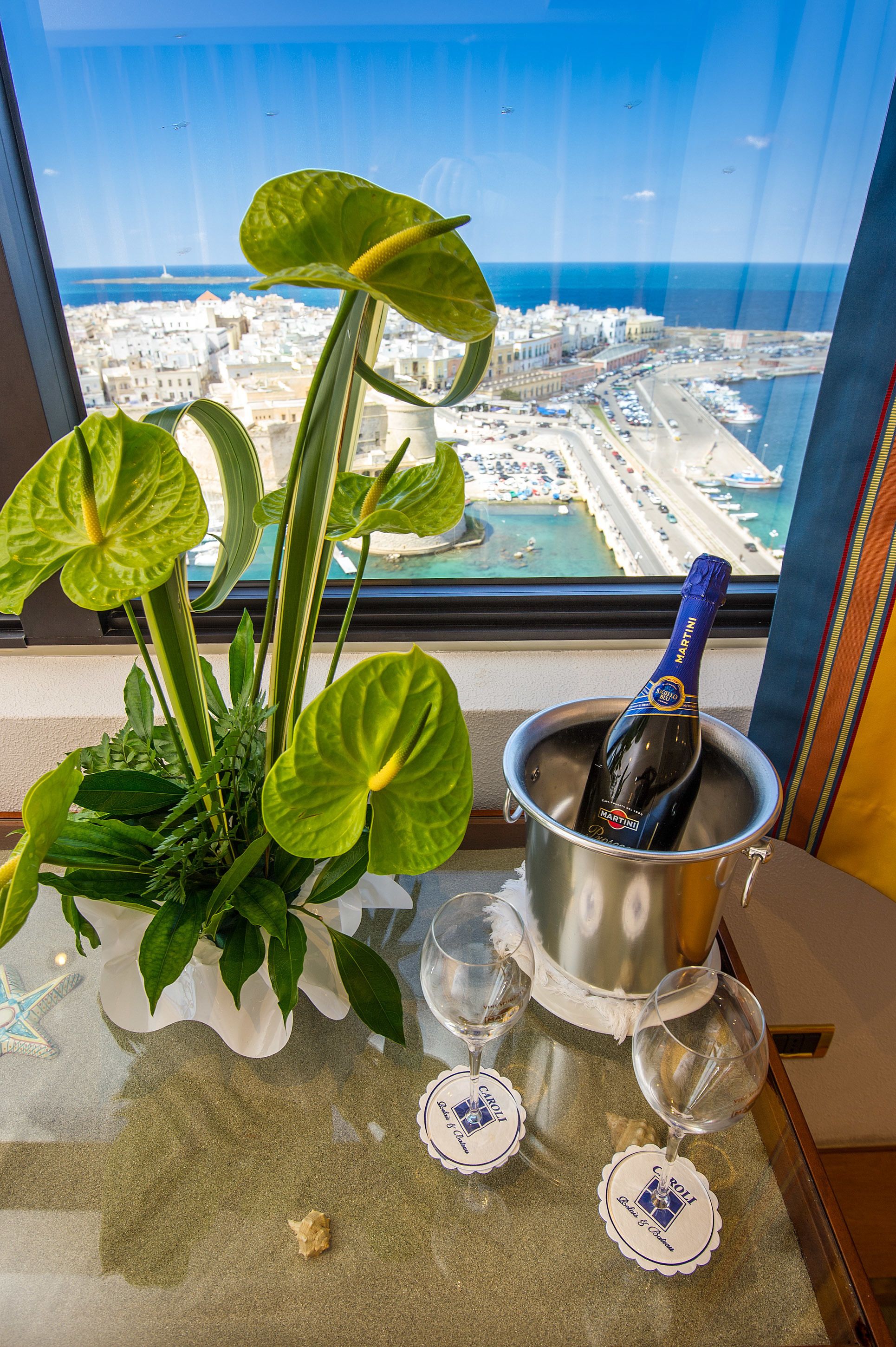A table with a plant, a bottle of champagne, and two glasses with coasters.