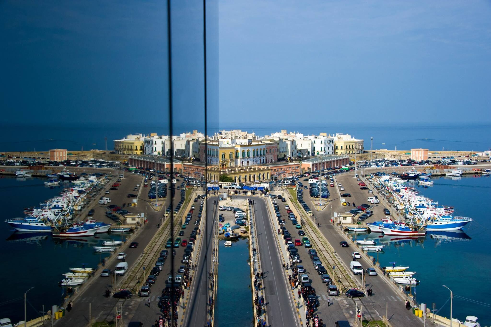 A harbor with boats docked, a central building with arches, and a road leading to the harbor.