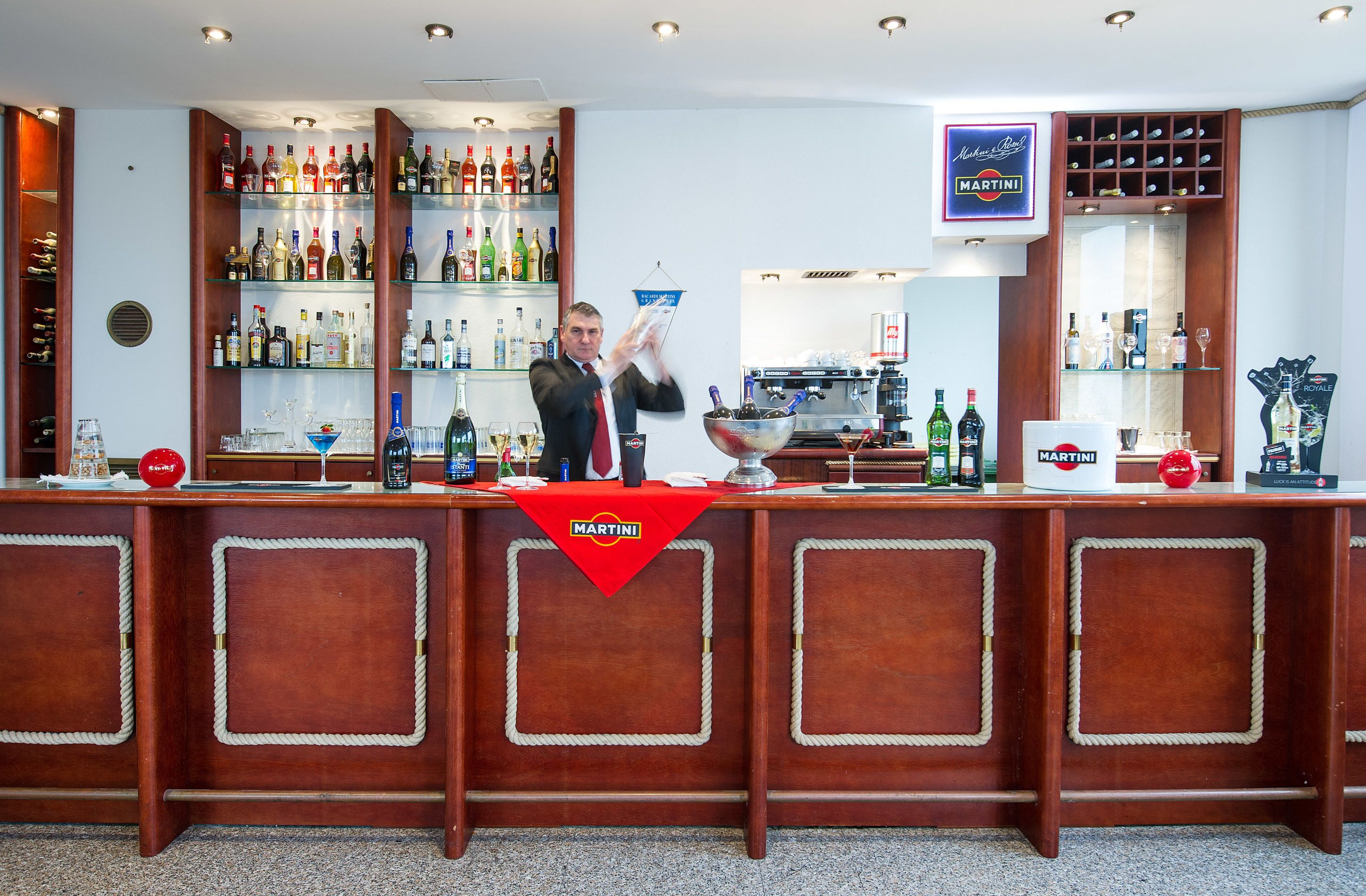 Zona de bar con un cantinero, estantes de licores y un cartel de Martini.