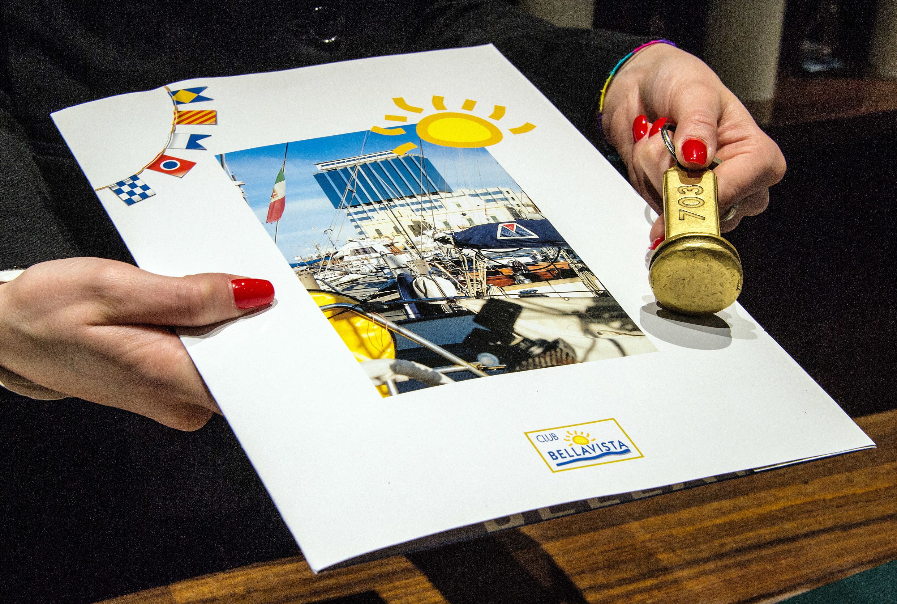 A person holding a booklet with a photograph of a marina and a sun illustration.