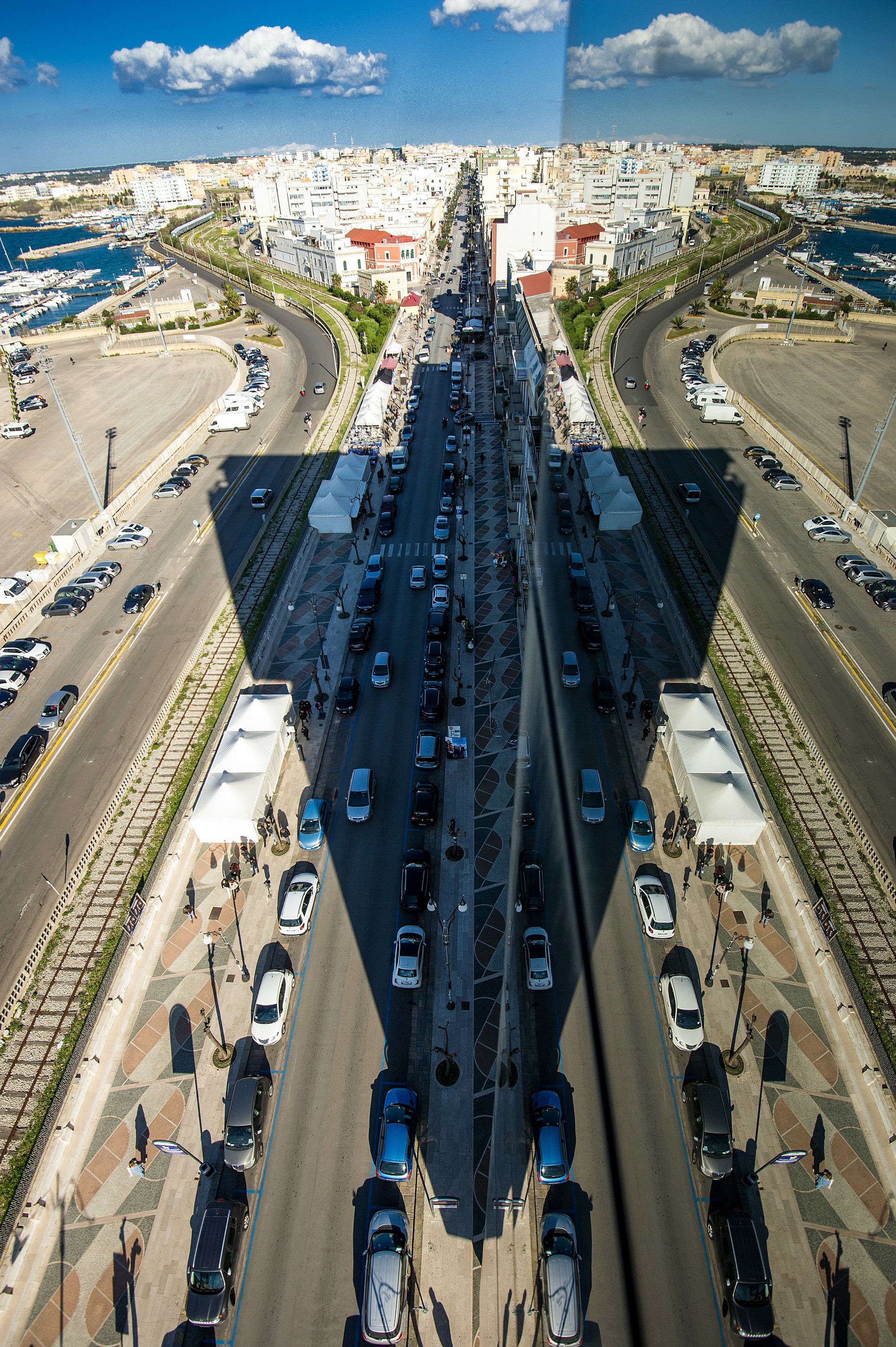 A busy urban intersection with multiple lanes of traffic and a marina in the background.