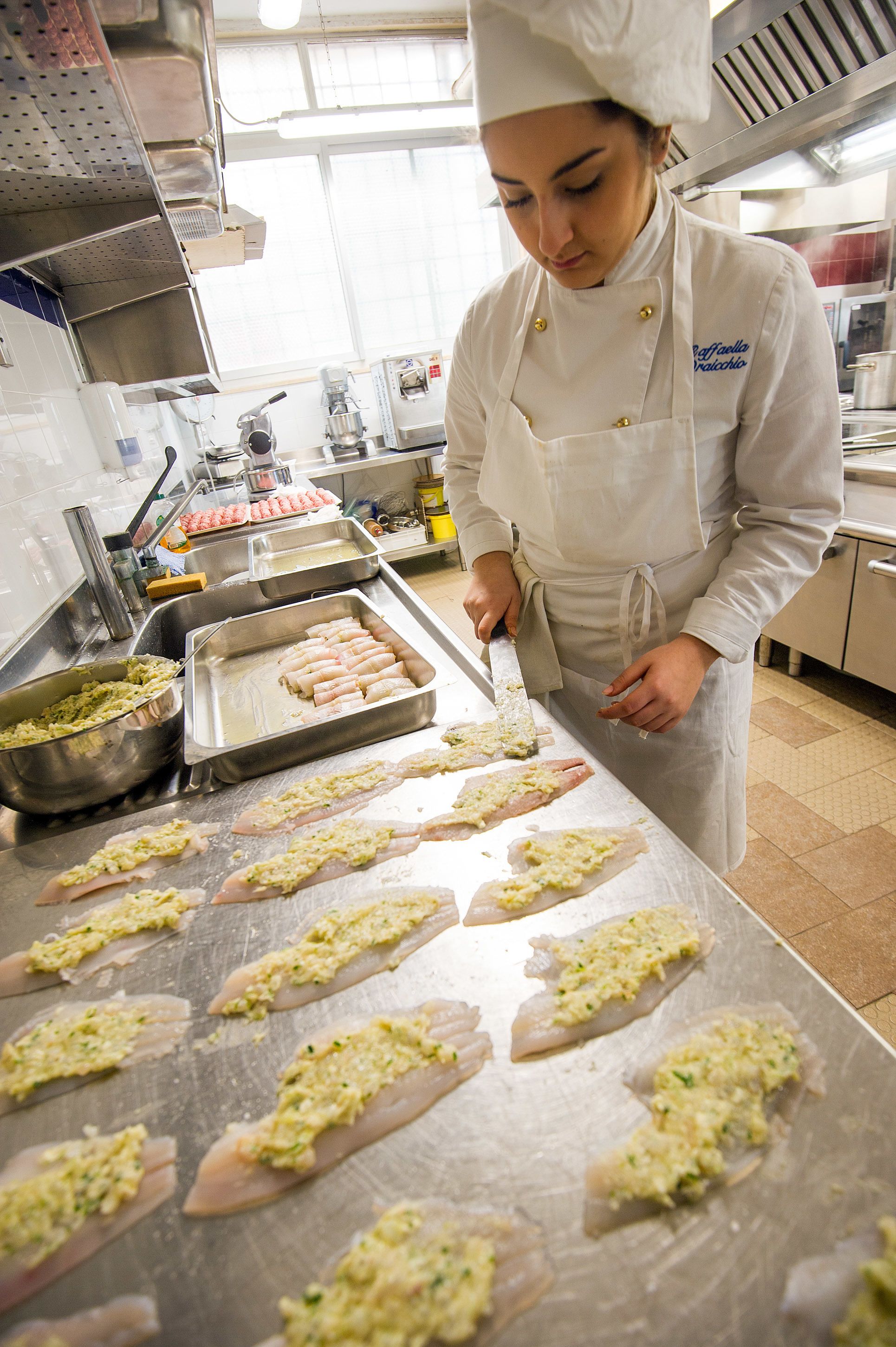 Een kok bereidt eten in een professionele keuken met roestvrijstalen oppervlakken en diverse kookapparatuur.