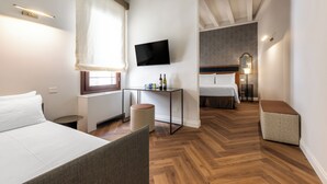 Une chambre d’hôtel moderne équipée d’un lit, d’une télévision, d’une petite table avec des bouteilles, d’une chaise et d’un banc.