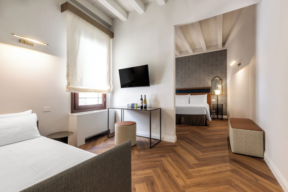 Una habitación de hotel moderna con una cama, un televisor, una mesita con botellas, una silla y un banco.