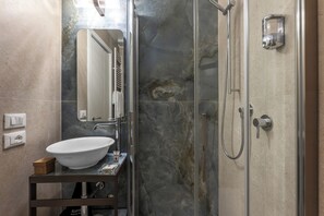 Une salle de bain avec un lavabo blanc, un miroir, un espace douche et un mur en marbre.