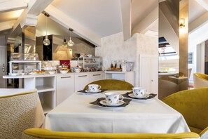 Un comedor con una mesa dispuesta para un servicio de té, una cocina al fondo y vistas de la ciudad.