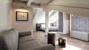 Une chambre d’hôtel moderne avec un lit en mezzanine, un canapé gris, une petite table ronde et un tableau encadré au mur.