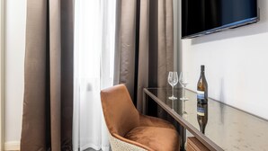 Une pièce avec un téléviseur fixé au mur, une table en verre avec une bouteille et des verres, et une chaise.