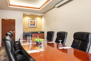 A conference room with a wooden table, black leather chairs, a bowl of green apples, and wine glasses. - Hampton Inn & Suites Denver - Cherry Creek (Glendale)