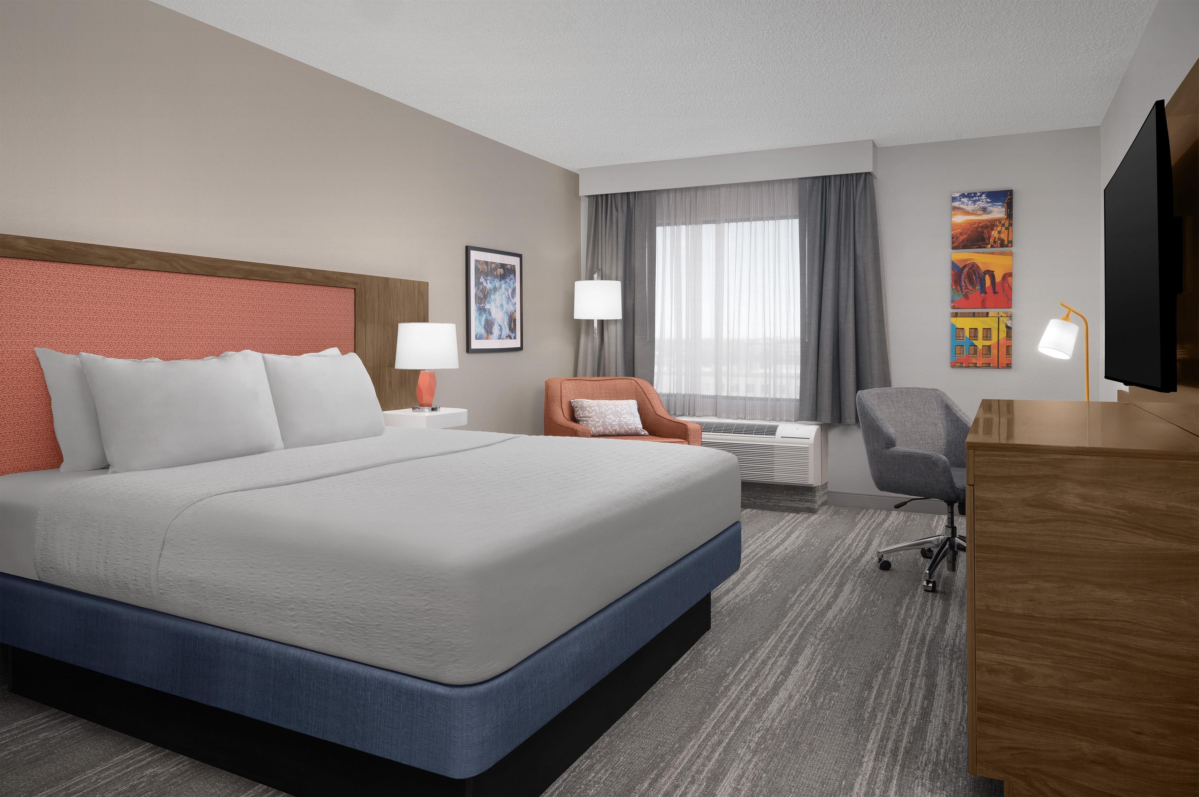 Quarto de hotel com uma cama grande, uma escrivaninha, uma cadeira e uma televisão.