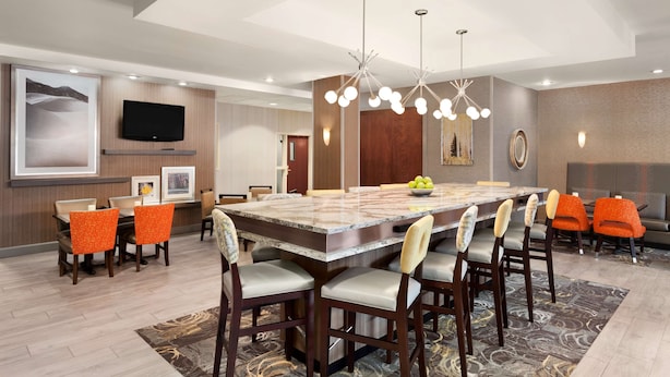 A spacious dining area with a large marble table, multiple chairs, and a modern chandelier. - Hampton Inn & Suites Denver - Cherry Creek (Glendale)