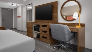 A hotel room with a bed, a desk with a TV, a mirror, and a lamp. - Hampton Inn & Suites Denver - Cherry Creek (Glendale)