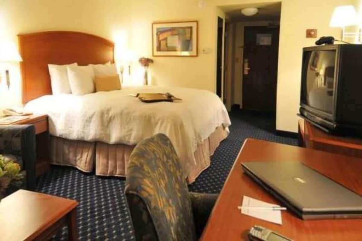 A hotel room with a bed, bedside table, lamp, desk, chair, laptop, and television.