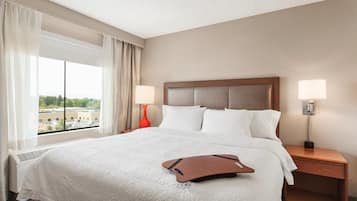 Habitación de hotel con una cama grande, dos lámparas de noche, una mesita de noche y un ventanal con cortinas.