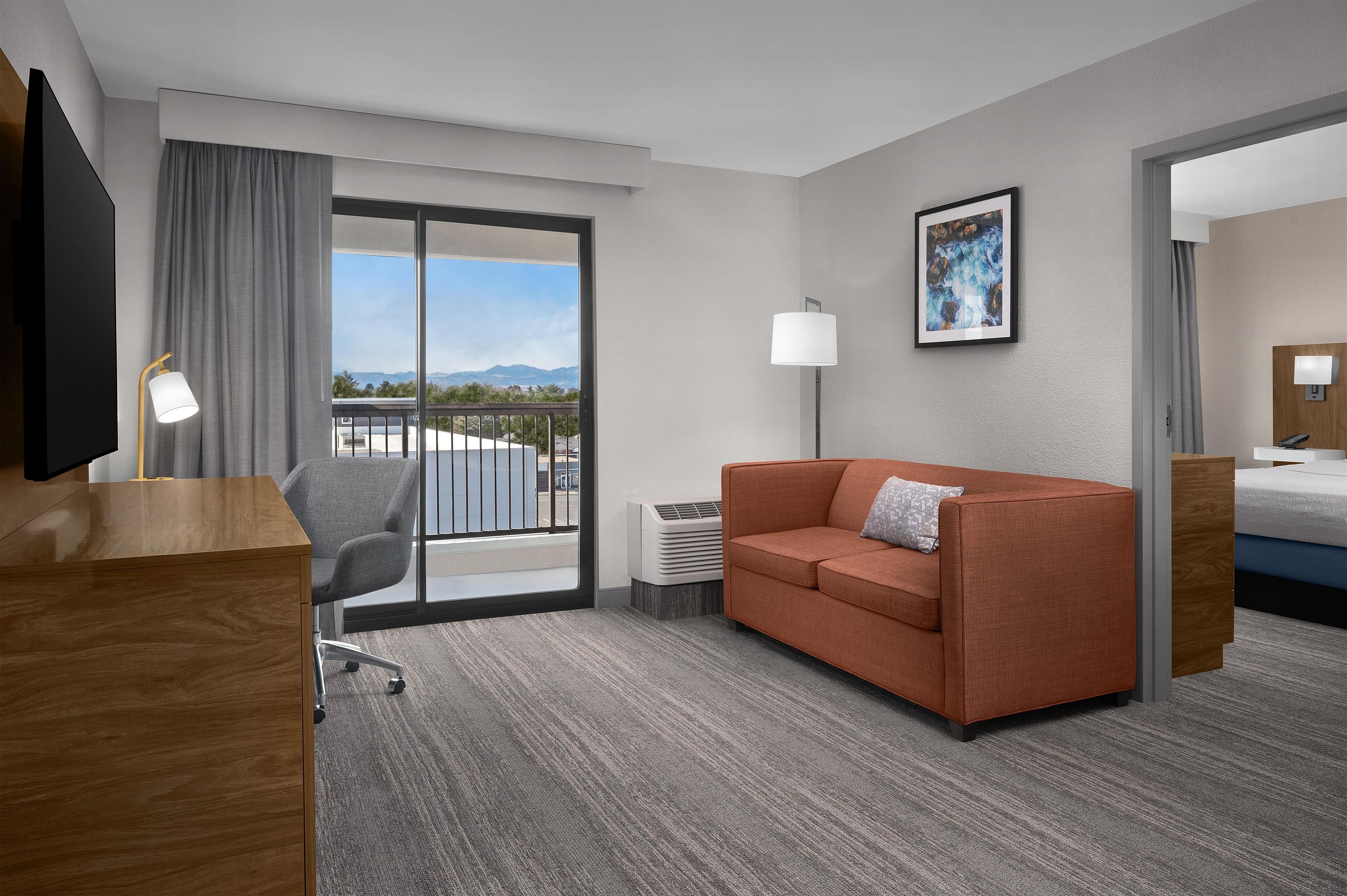 A hotel room with a sofa, a desk, a chair, a bed, a TV, a lamp, and a painting on the wall.