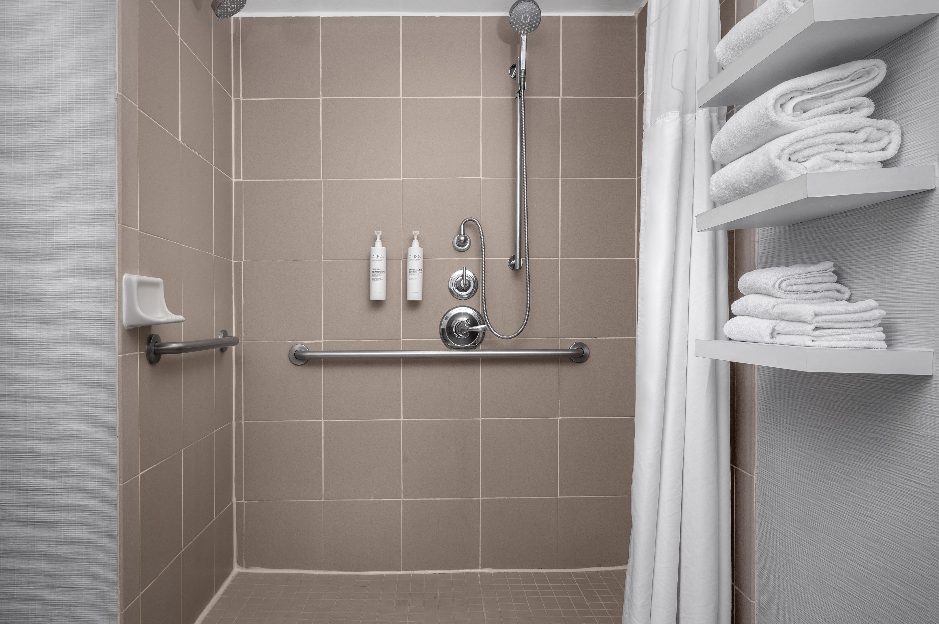 A shower area with a grab bar, a towel rack, and a shelf with folded towels.