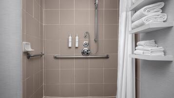 A shower area with a grab bar, a towel rack, and a shelf with folded towels.