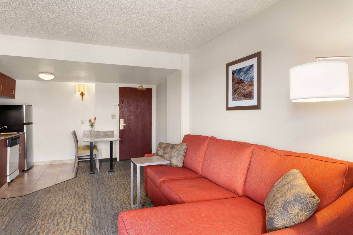 A compact living space with a red sofa, a small dining table, a kitchen area, and a framed picture on the wall.