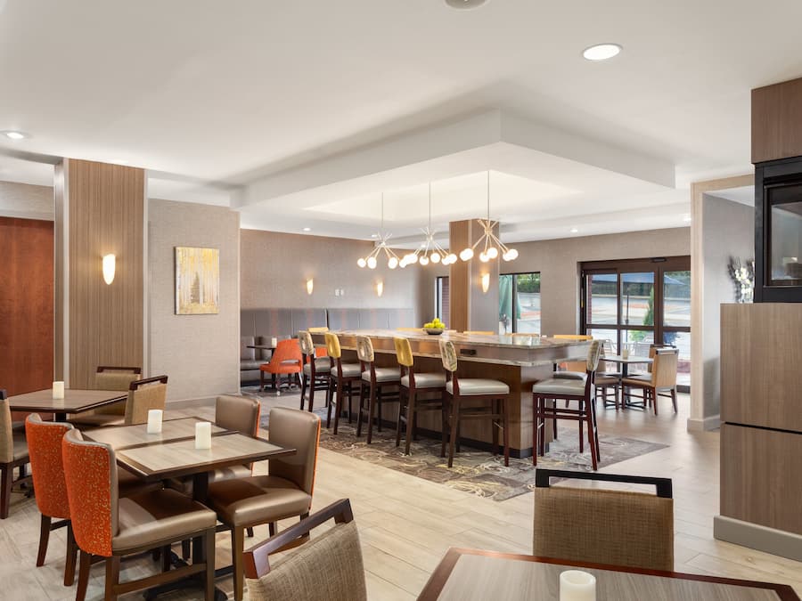 Un comedor de hotel moderno con varias mesas y sillas, una isla central con barra, y una zona de cocina a la derecha.
