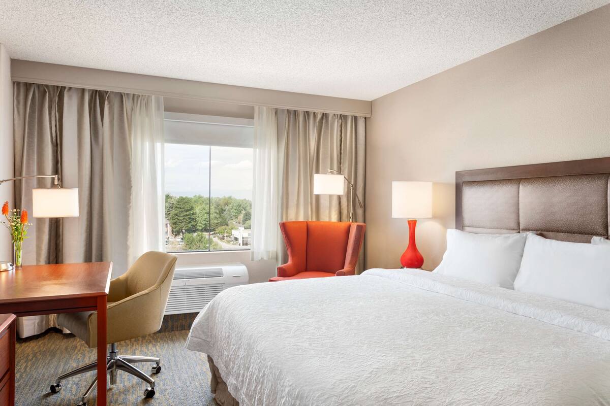 A hotel room with a large bed, a desk, a chair, and a window with curtains.