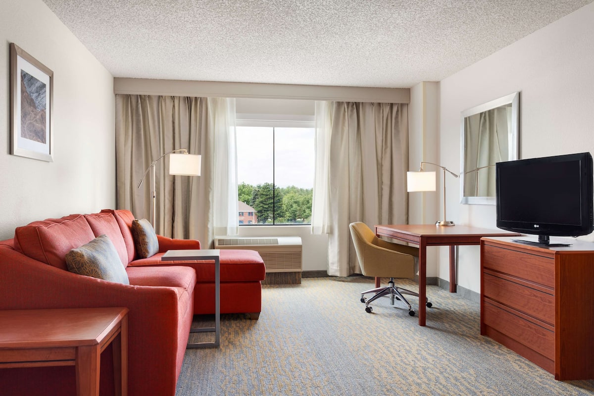 A hotel room with a red sofa, a wooden desk, a television, and a window with curtains.