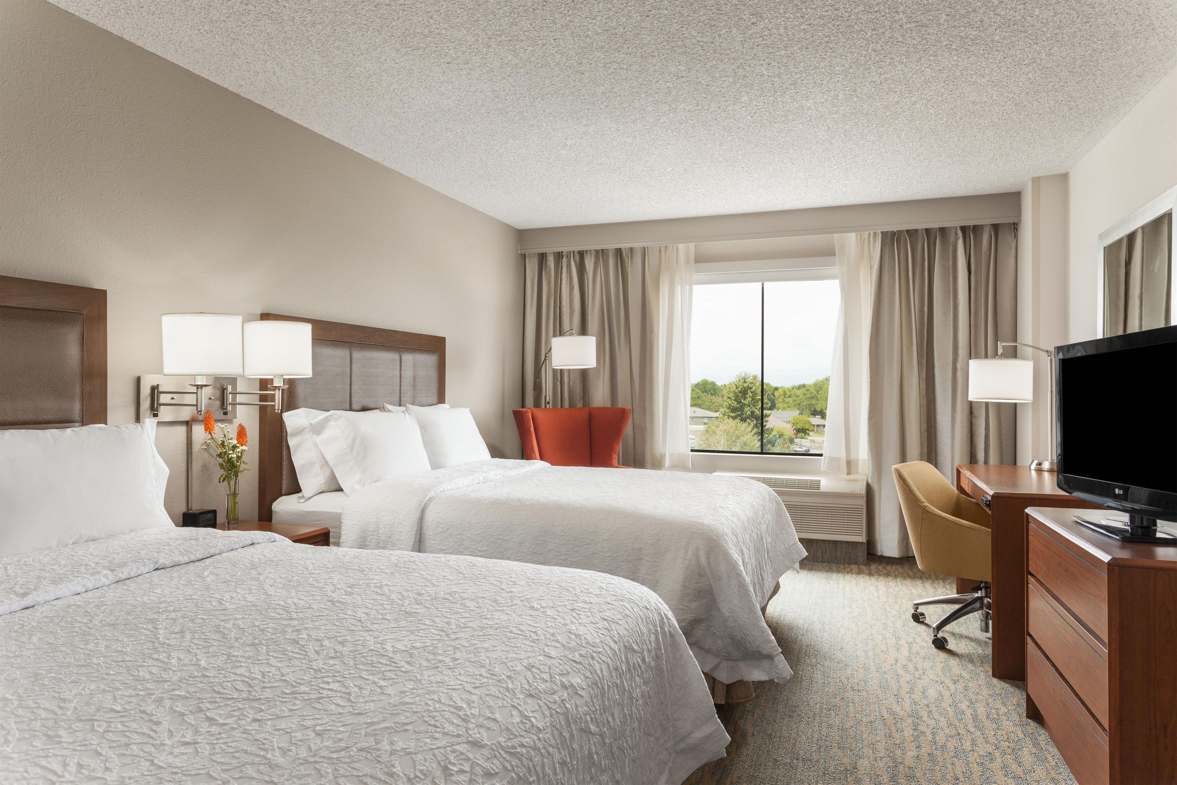 A hotel room with two beds, a desk, a TV, and a window with a view.
