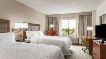 A hotel room with two beds, a desk, a TV, and a window with a view.