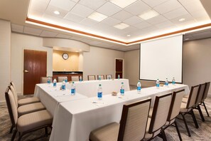 A conference room with a long table, chairs, a clock, and a projector screen. - Hampton Inn & Suites Denver - Cherry Creek (Glendale)