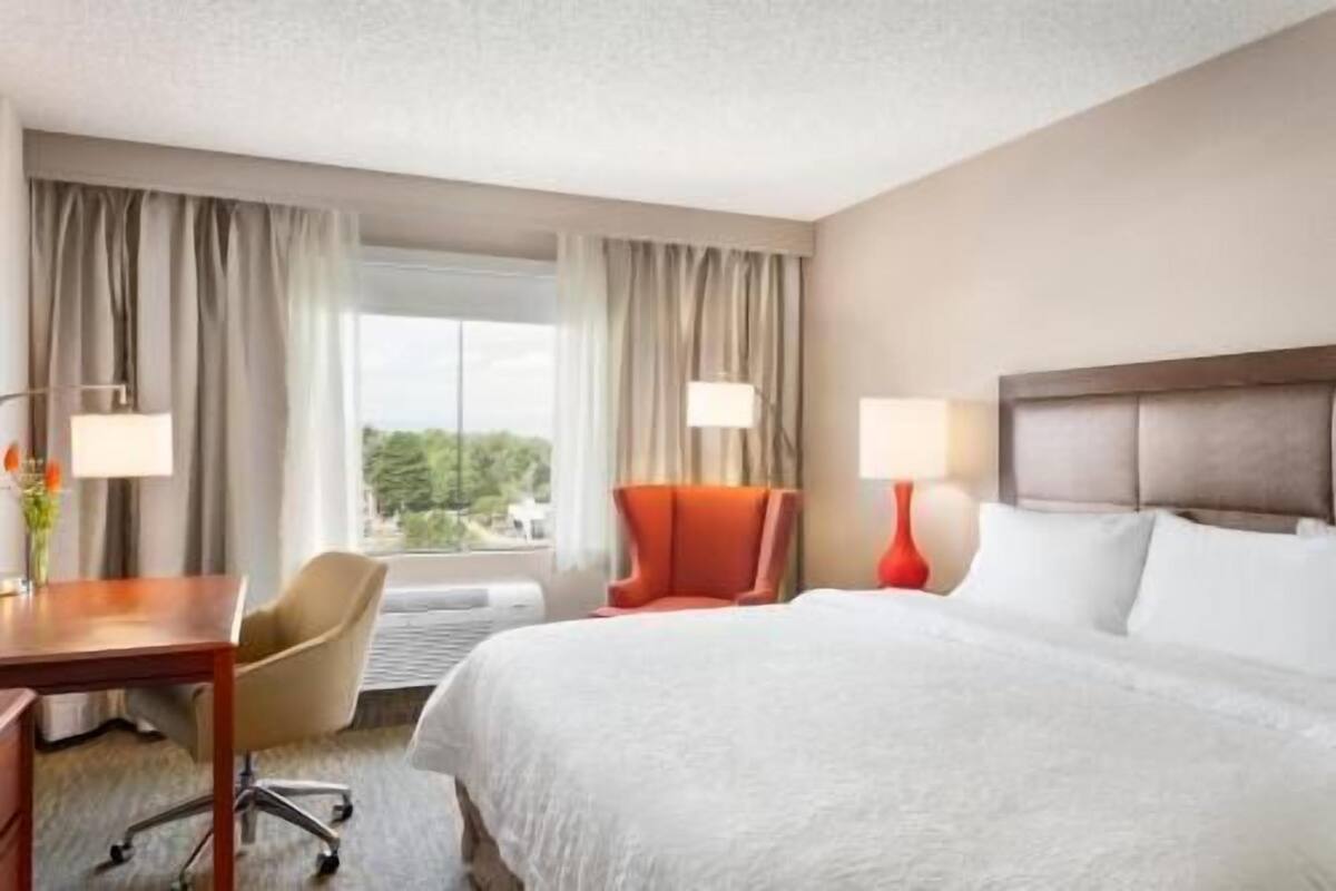A hotel room with a bed, a desk, a chair, and a window with curtains.