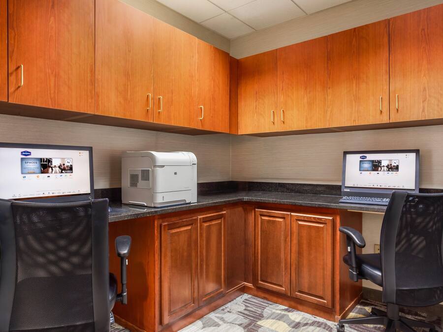 Un petit bureau avec des armoires en bois, deux bureaux équipés d’ordinateurs et une machine à café.