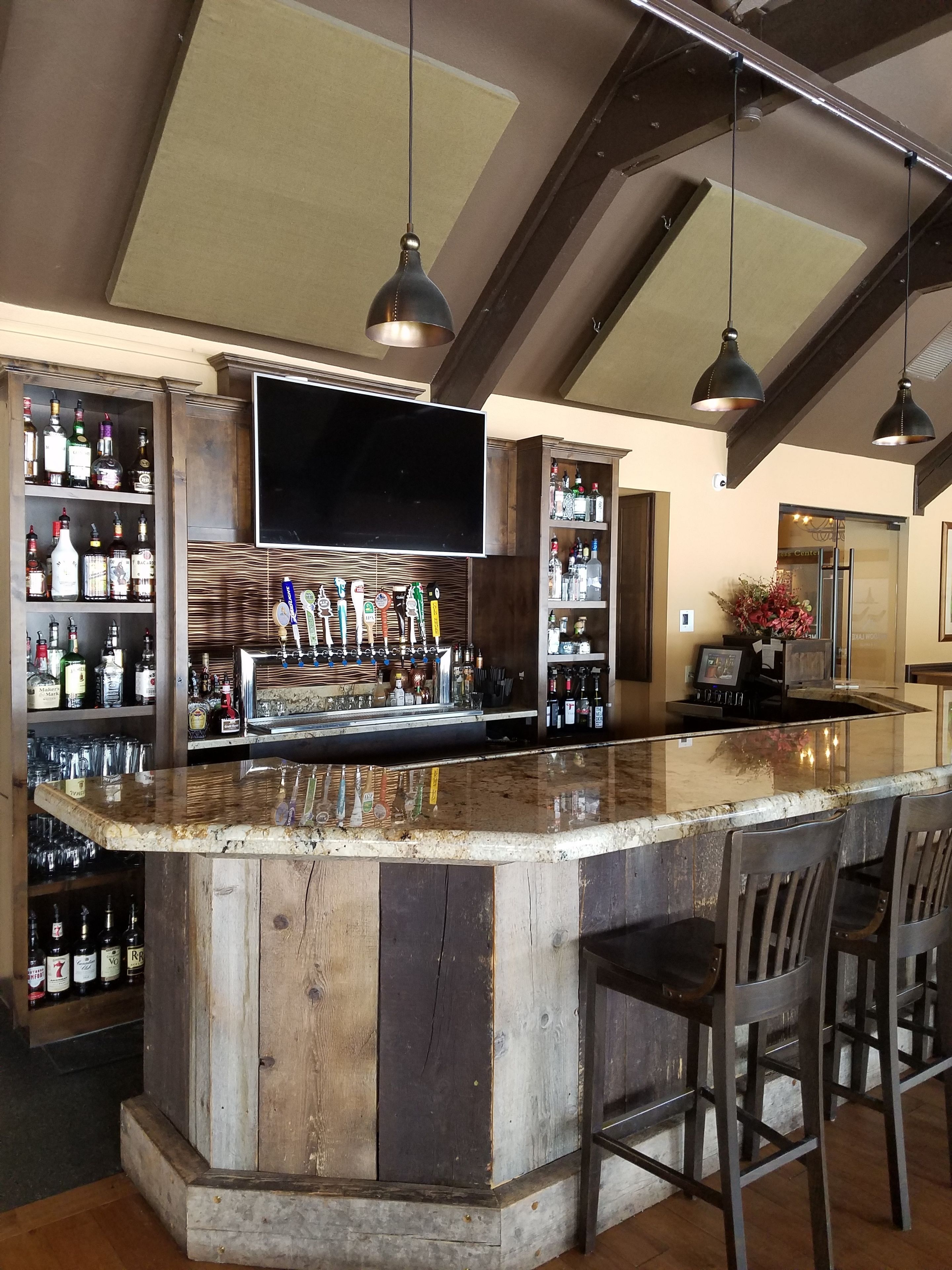 Een bar met een houten toog, diverse drankflessen en een flatscreen televisie boven de toog.