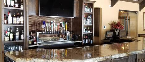 Een bar met een houten toog, diverse drankflessen en een flatscreen televisie boven de toog.