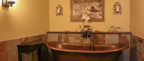 Une salle de bain avec une baignoire sur pieds, une petite table, un luminaire fixé au mur et un tableau encadré au-dessus de la baignoire.