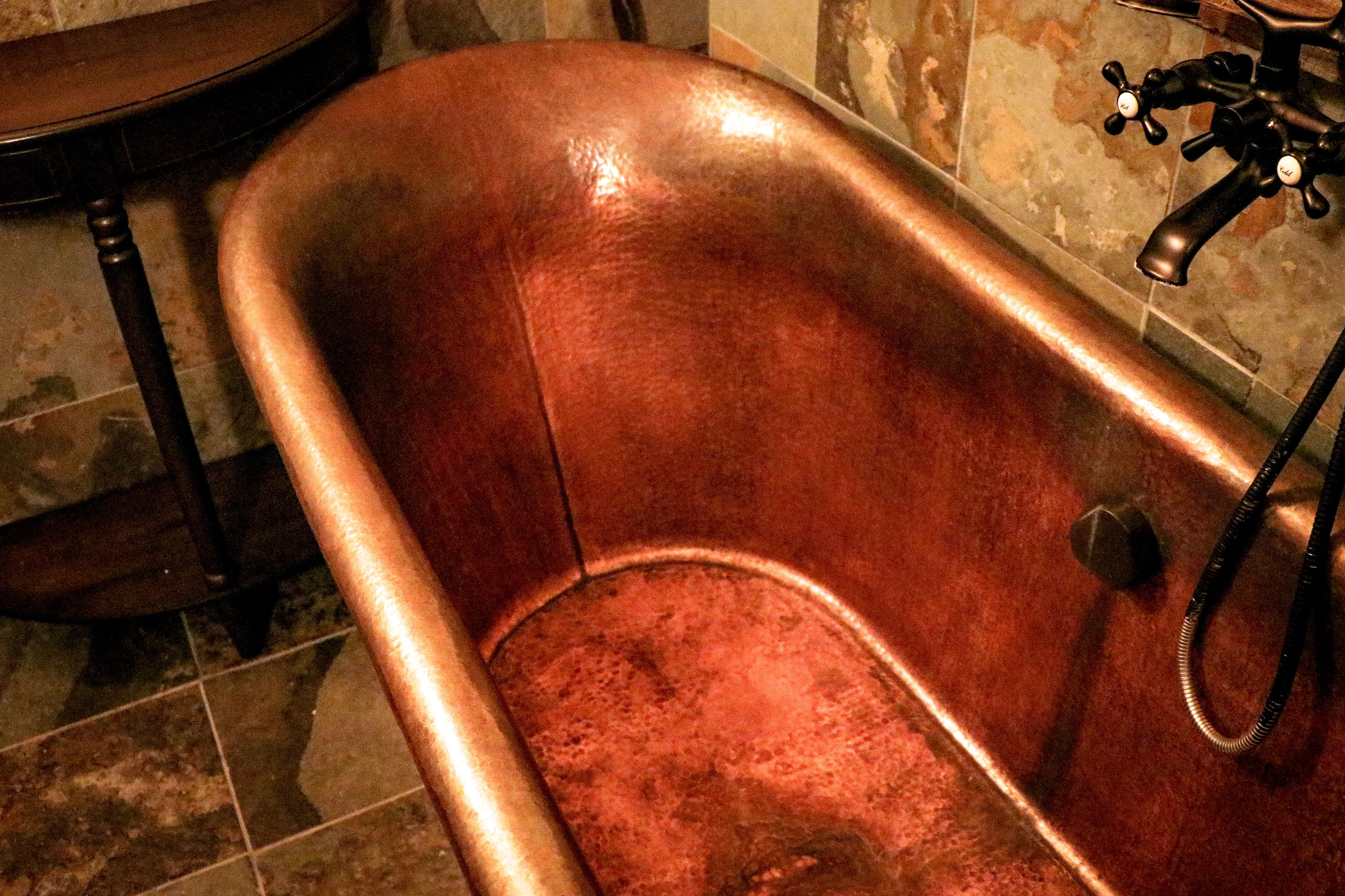 A copper bathtub with a faucet and hose.