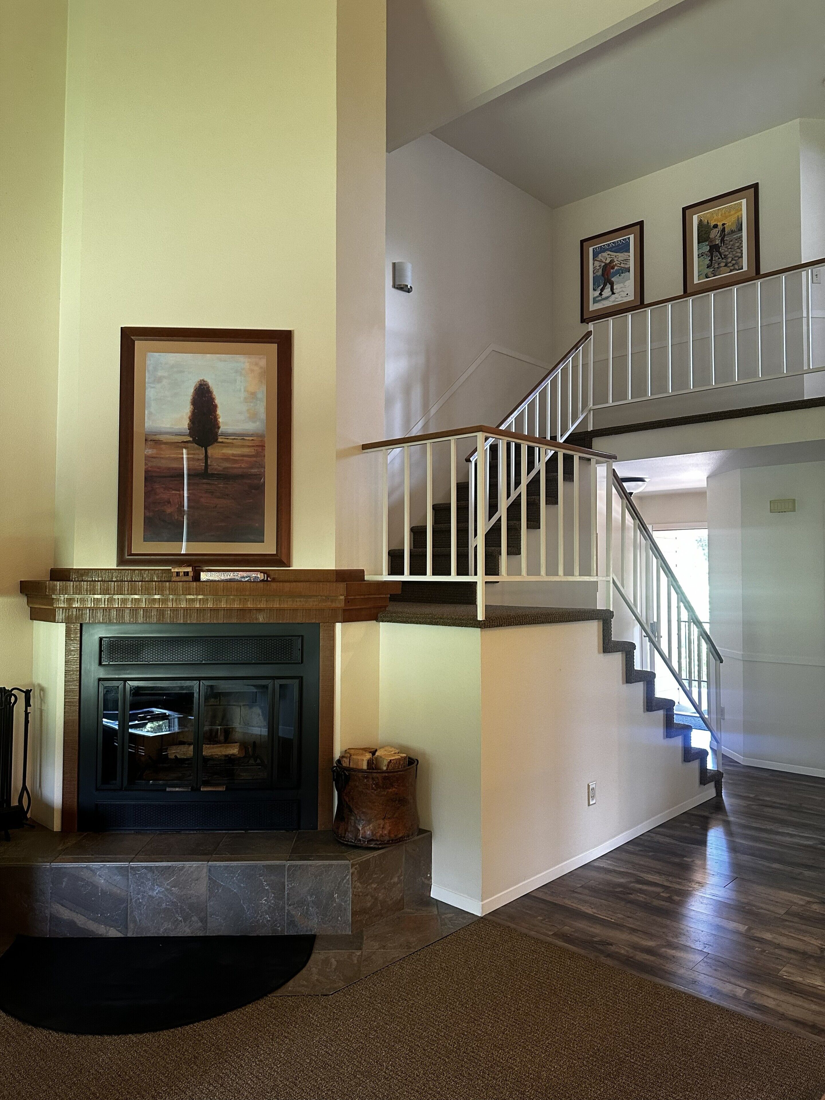 A spacious living area with a fireplace, a staircase, and framed artwork on the walls.