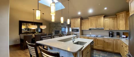 A modern kitchen with a central island, bar stools, wooden cabinets, a stone accent wall, and pendant lighting.