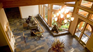 A spacious room with a checkered floor, a large potted plant, a wooden bench, and a staircase leading to an upper level. - Meadow Lake Resort & Condos (Columbia Falls)