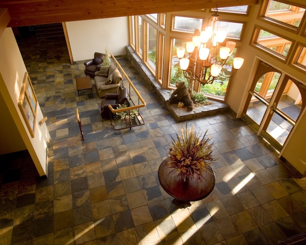 A spacious room with a checkered floor, a large potted plant, a wooden bench, and a staircase leading to an upper level. - Meadow Lake Resort & Condos (Columbia Falls)
