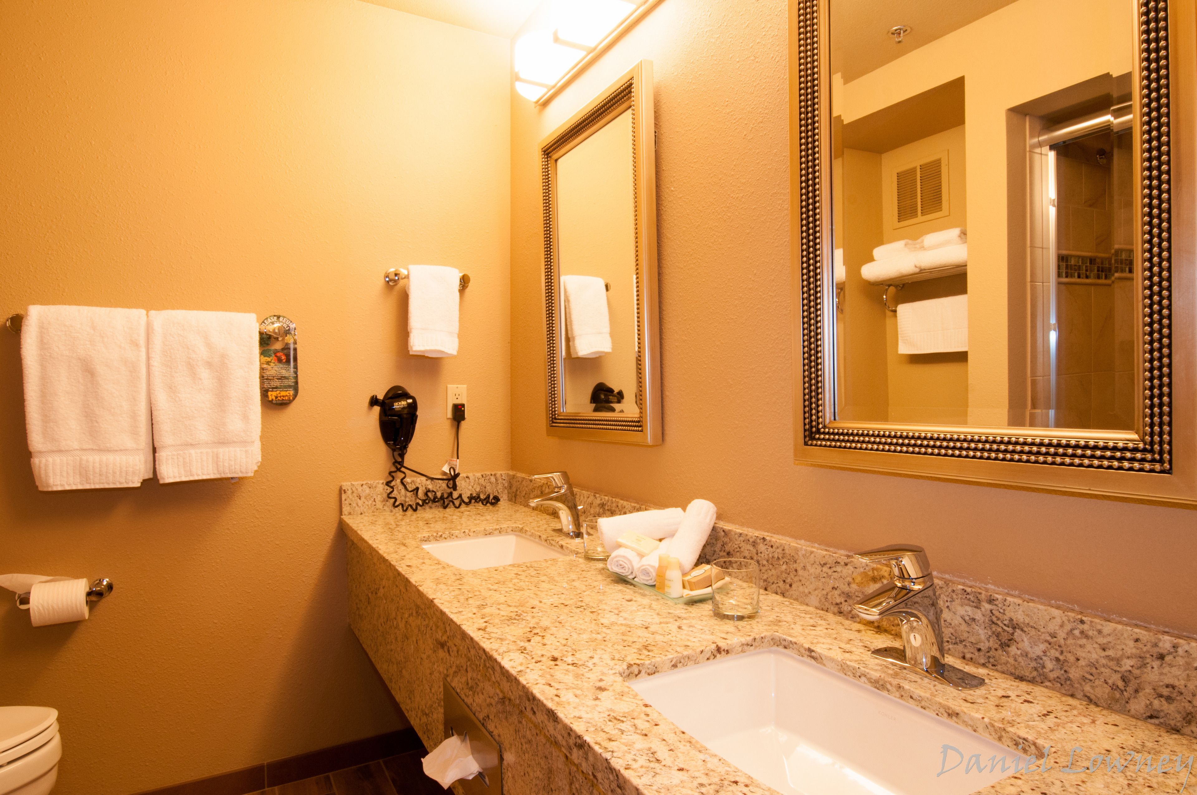 A hotel bathroom with two sinks, a large mirror, and towels on the wall.