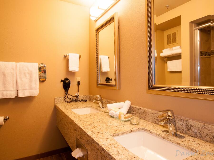 A hotel bathroom with two sinks, a large mirror, and towels on the wall.