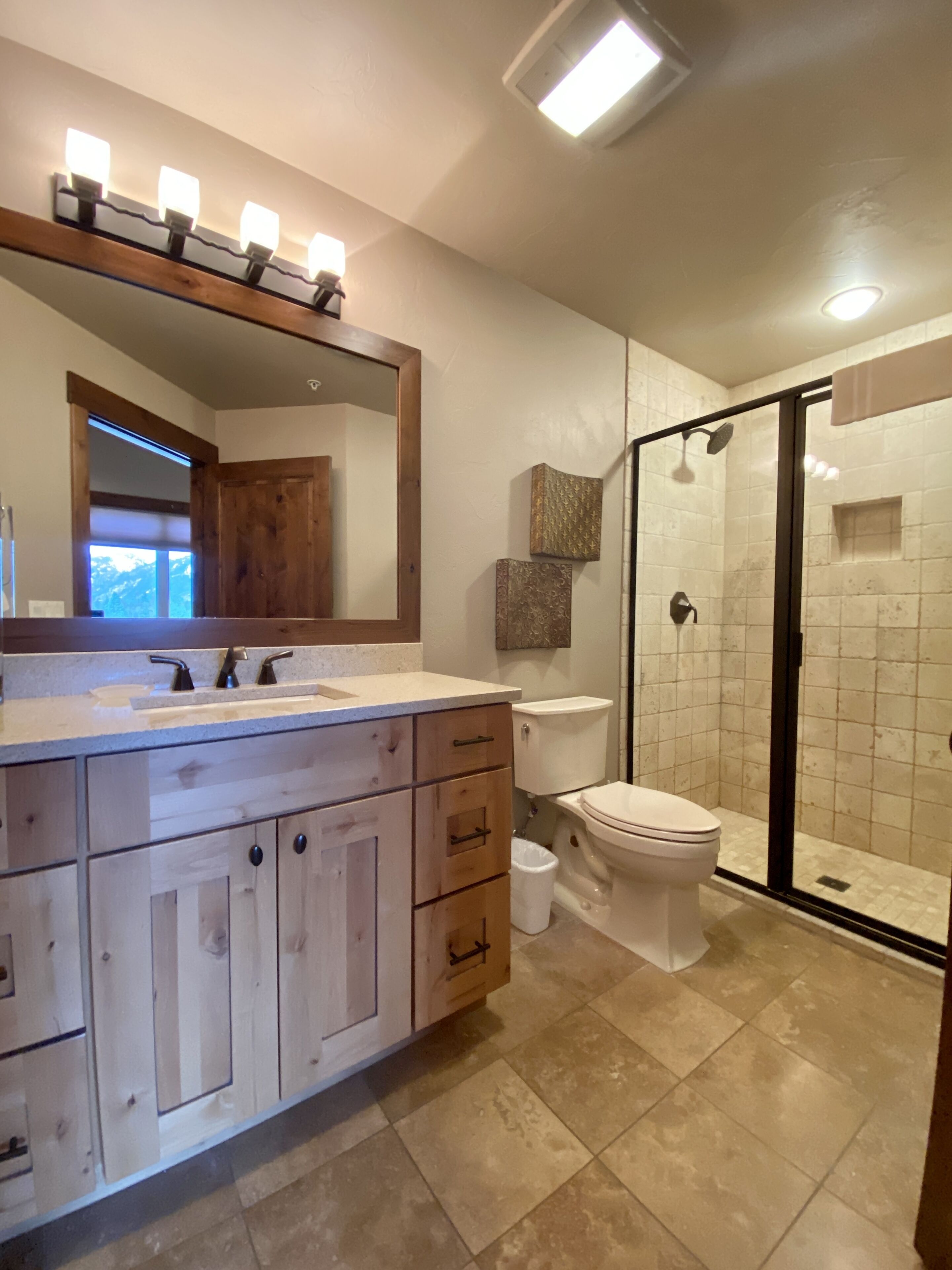 A modern bathroom with a wooden vanity, a large mirror, a toilet, and a glass-enclosed shower.