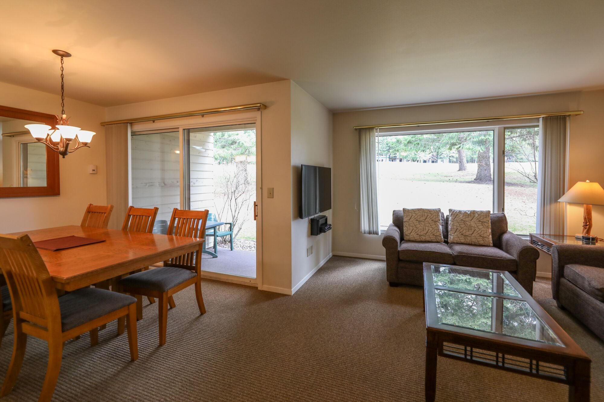 A spacious living room with a wooden dining table, chairs, a sofa, a glass coffee table, and a television.