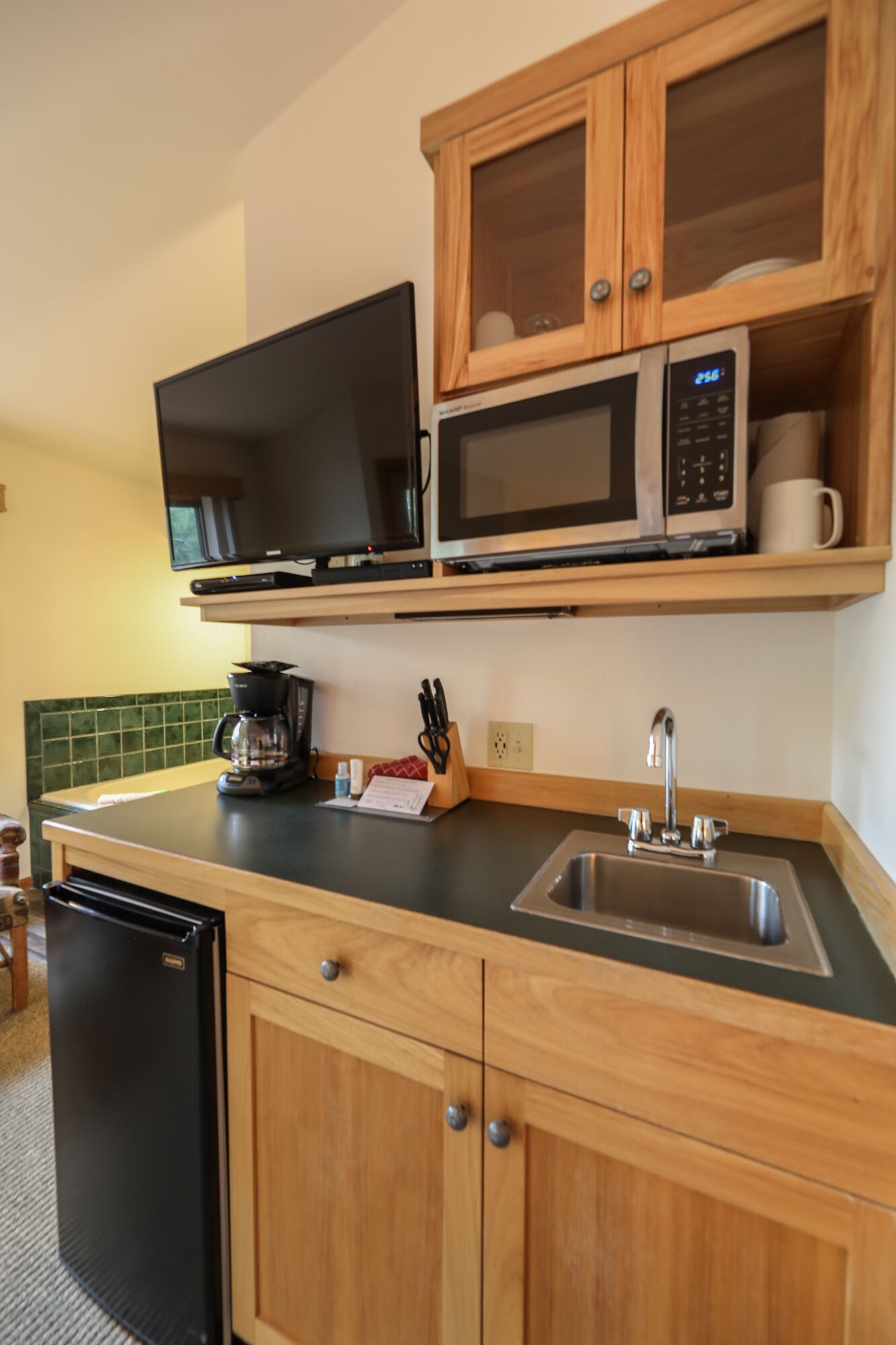 A compact kitchen with wooden cabinets, a microwave, a coffee maker, and a dishwasher.