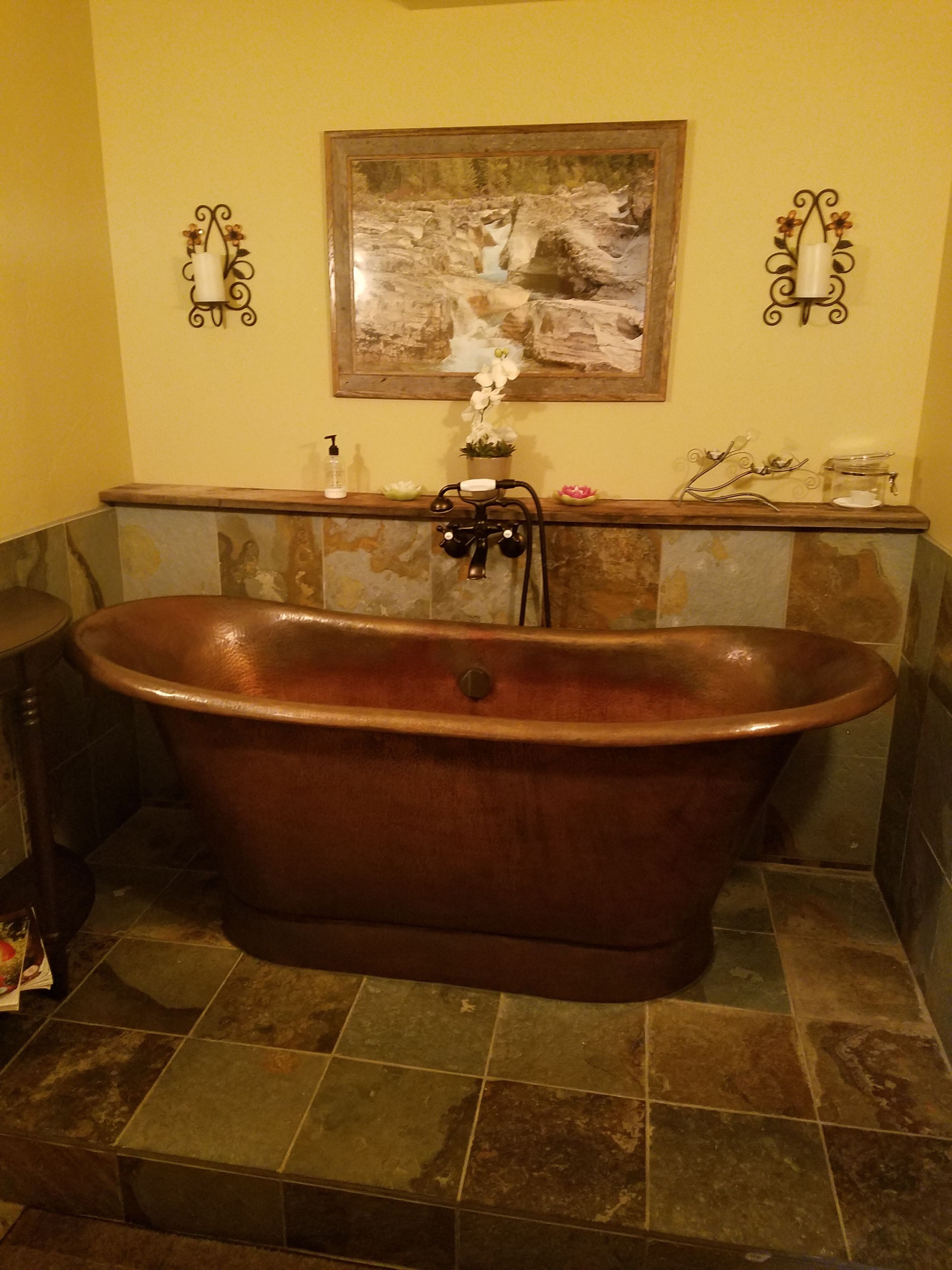 A bathroom with a freestanding bathtub, a framed artwork above the tub, and a shelf with toiletries.