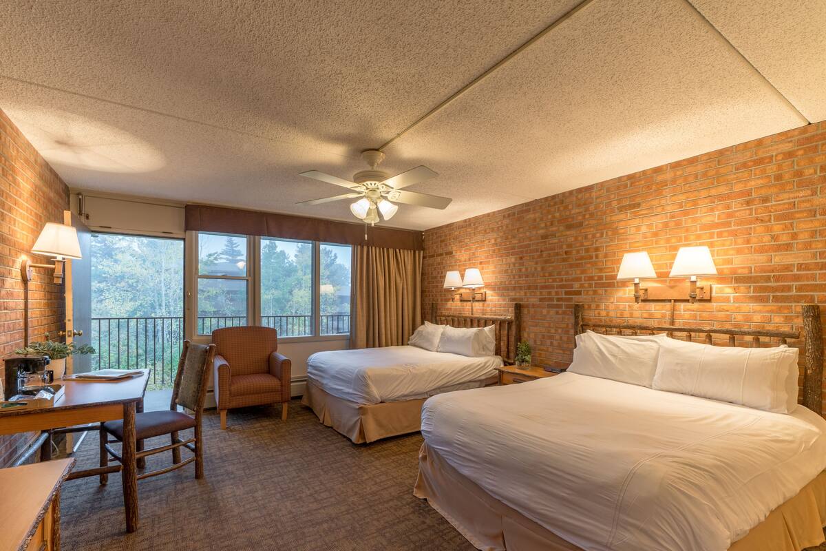 Une chambre d’hôtel avec deux lits, un bureau, une chaise, un ventilateur de plafond et une vue sur l’extérieur.