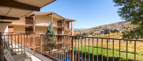 Un balcón con vista a un paisaje montañoso, una piscina y mobiliario de exterior.