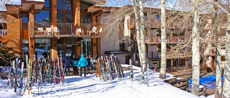 A ski resort building with multiple balconies and a ski rack filled with skis.