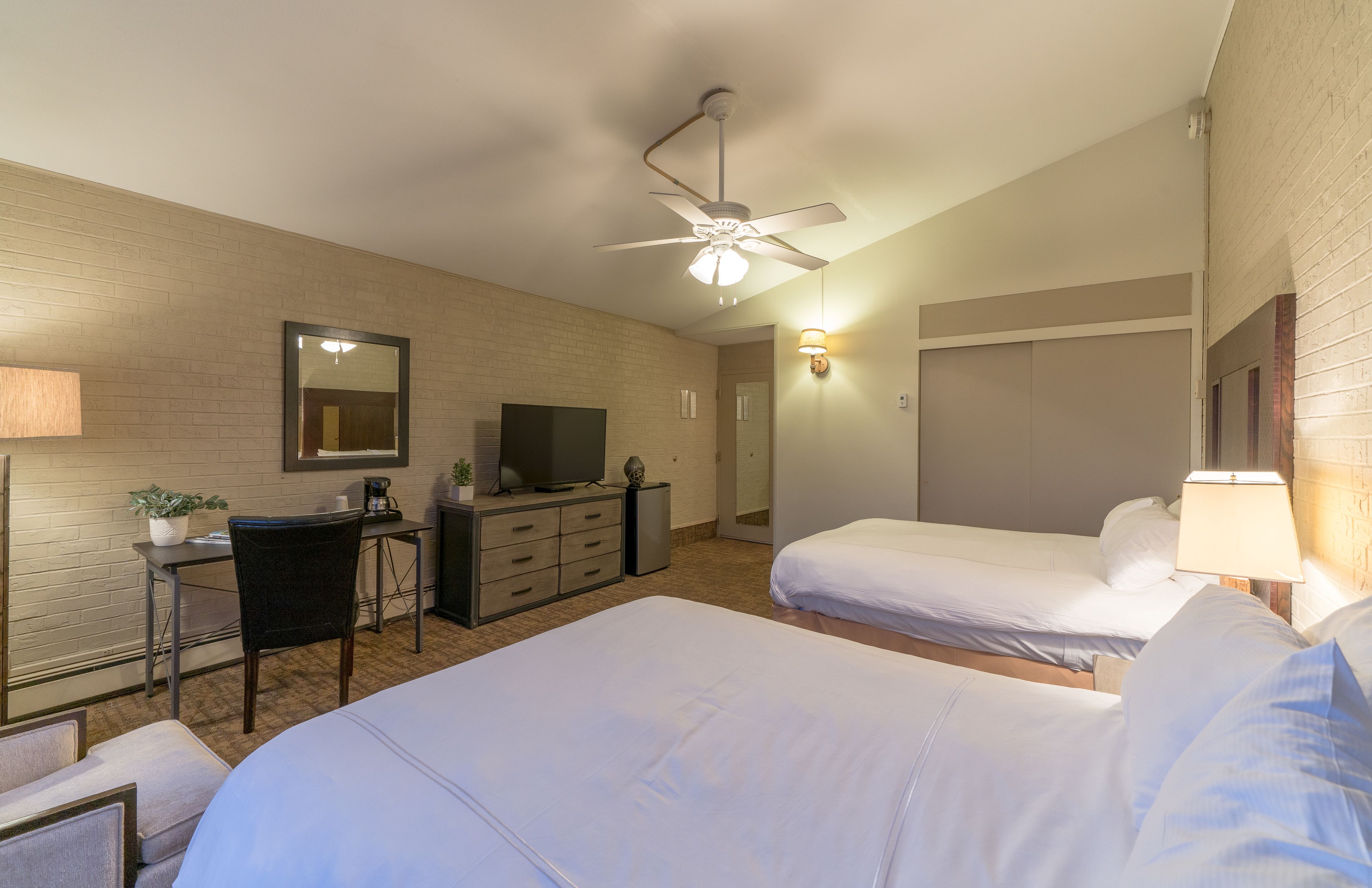 Habitación de hotel con dos camas, un escritorio con silla, televisor y ventilador de techo.