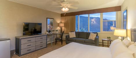 Ein Hotelzimmer mit Bett, Schreibtisch mit Computer, Fernseher, Sofa und Blick auf die Berge.